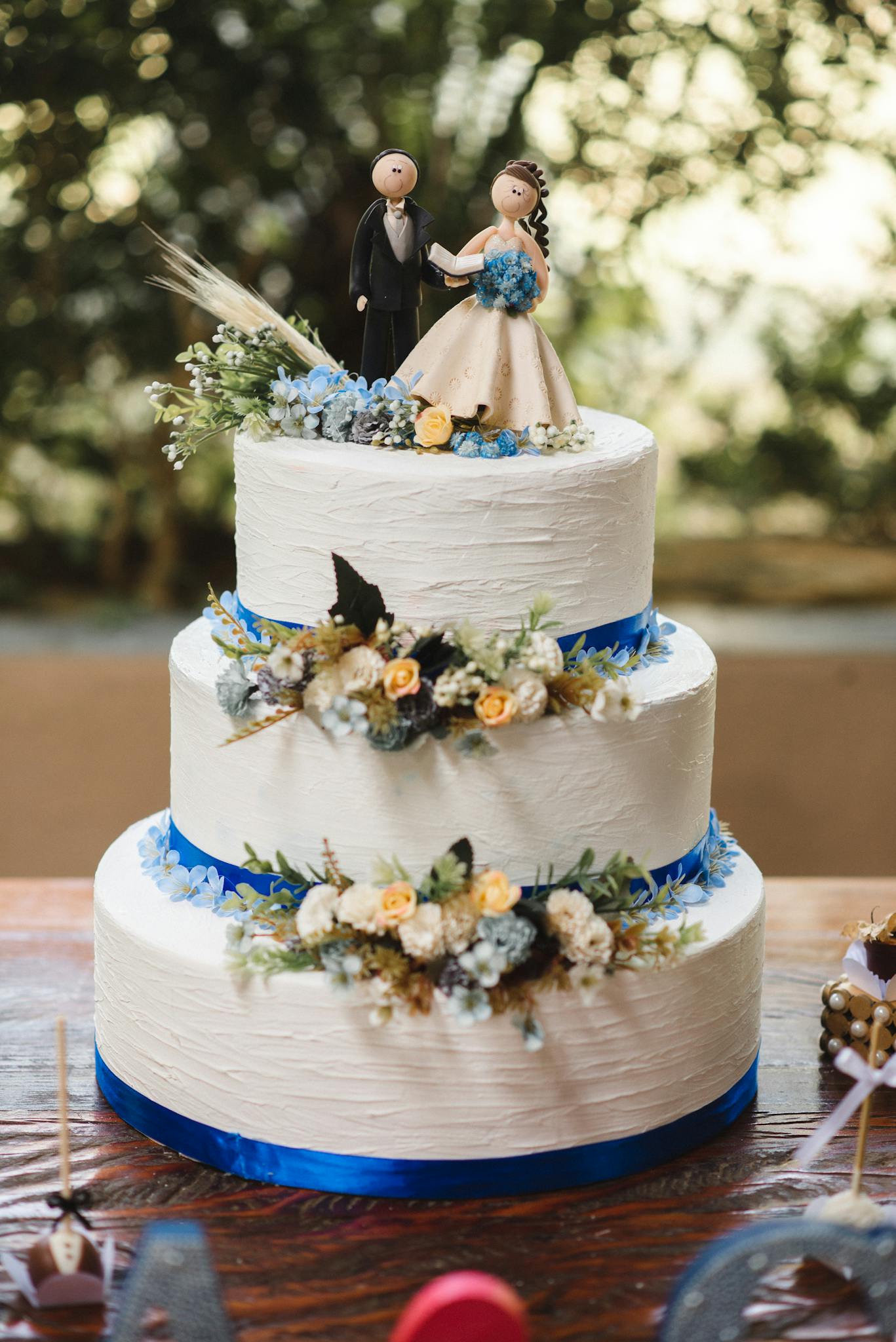 Elegant wedding cake with floral decorations and bride and groom figurines on top.